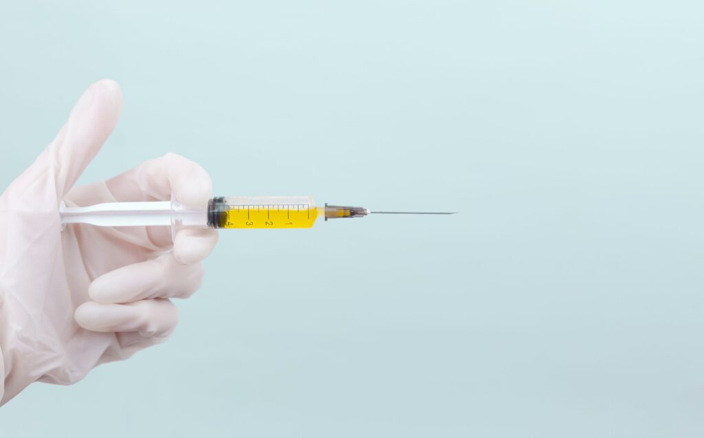 doctor's hand in a white medical glove holds a syringe with a yellow medicine on a blue background.